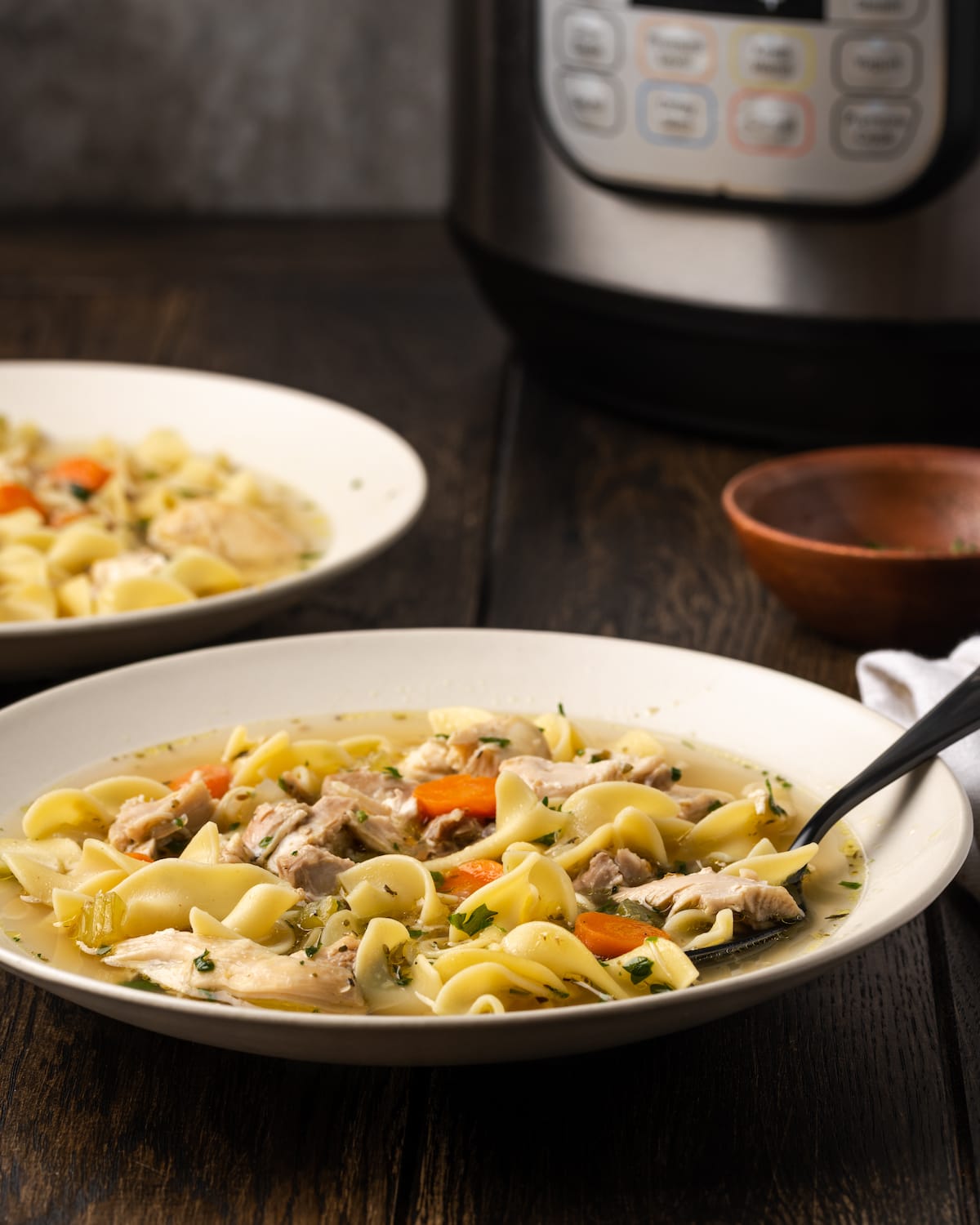 A bowl of Instant Pot chicken noodle soup, with a second bowl as well as the Instant Pot in the background.