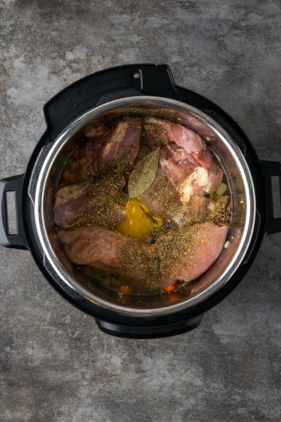 Uncooked chicken and seasonings added to sauteed veggies inside the Instant Pot.