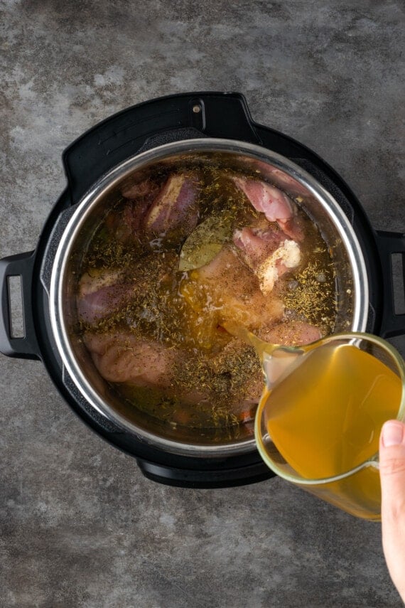Broth is poured over uncooked chicken and seasonings added to sauteed veggies inside the Instant Pot.