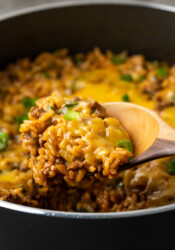 A wooden spoon scooping cheesy taco rice from a skillet.