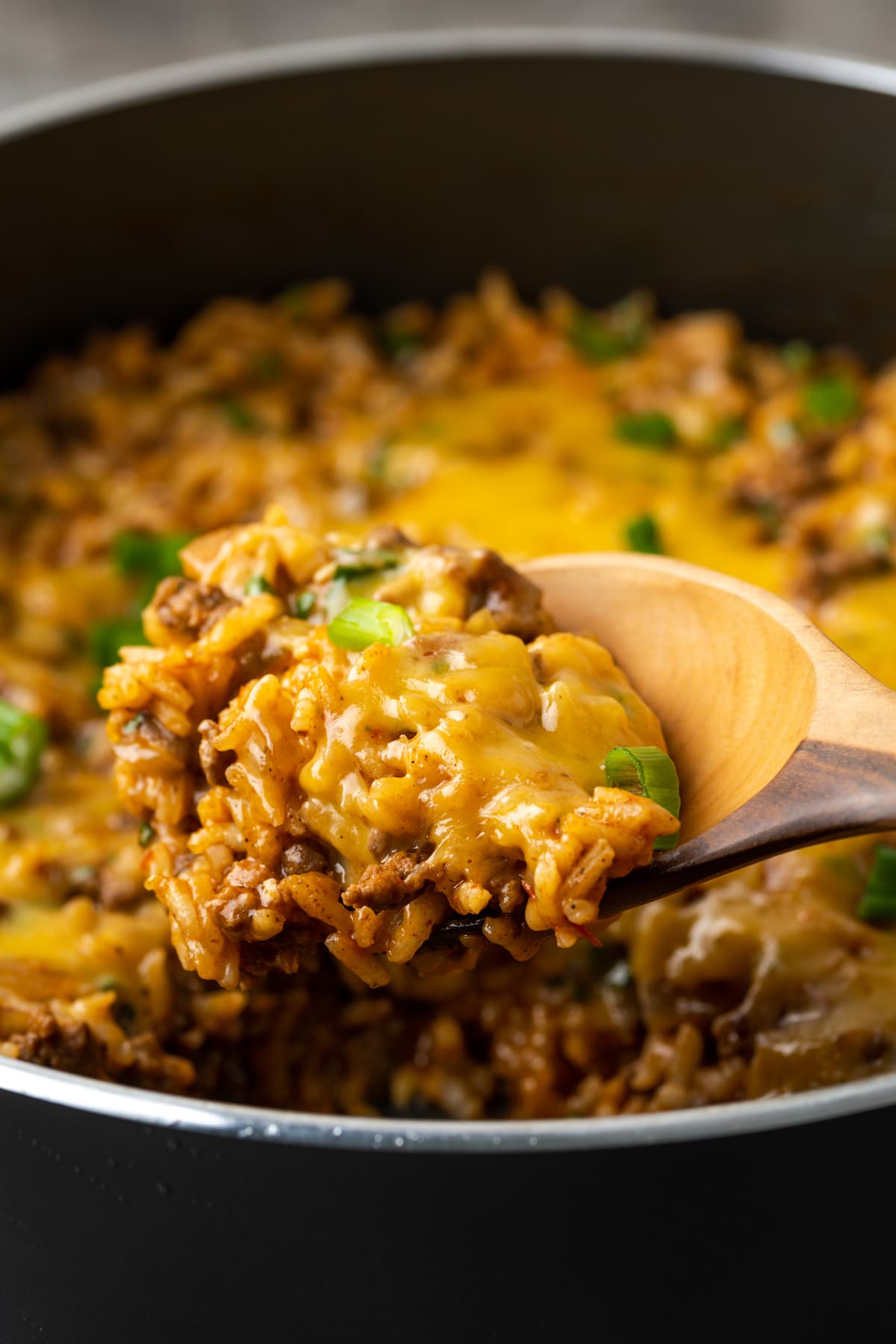 A wooden spoon scooping cheesy taco rice from a skillet.