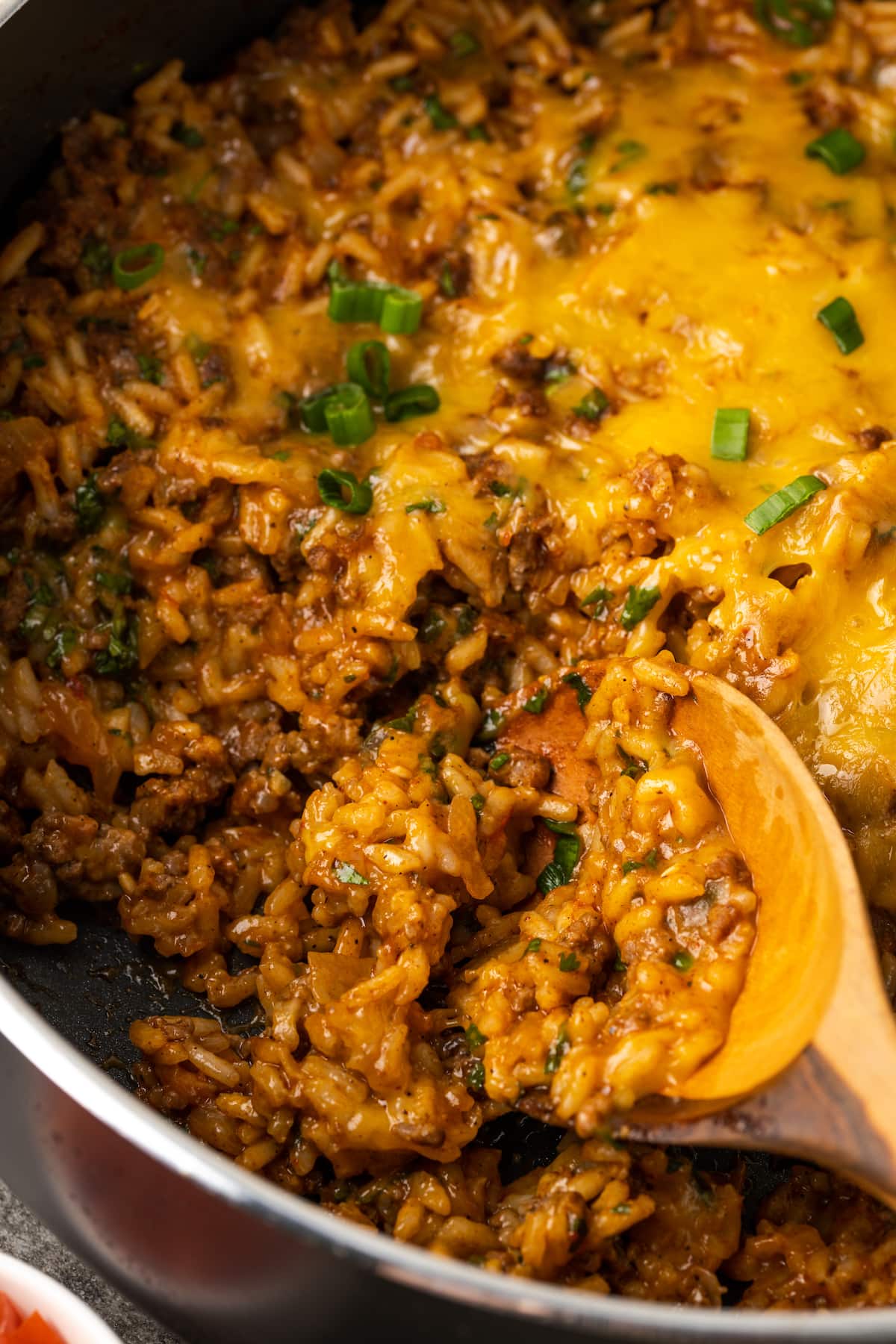 A wooden spoon scooping cheesy taco rice from a skillet.