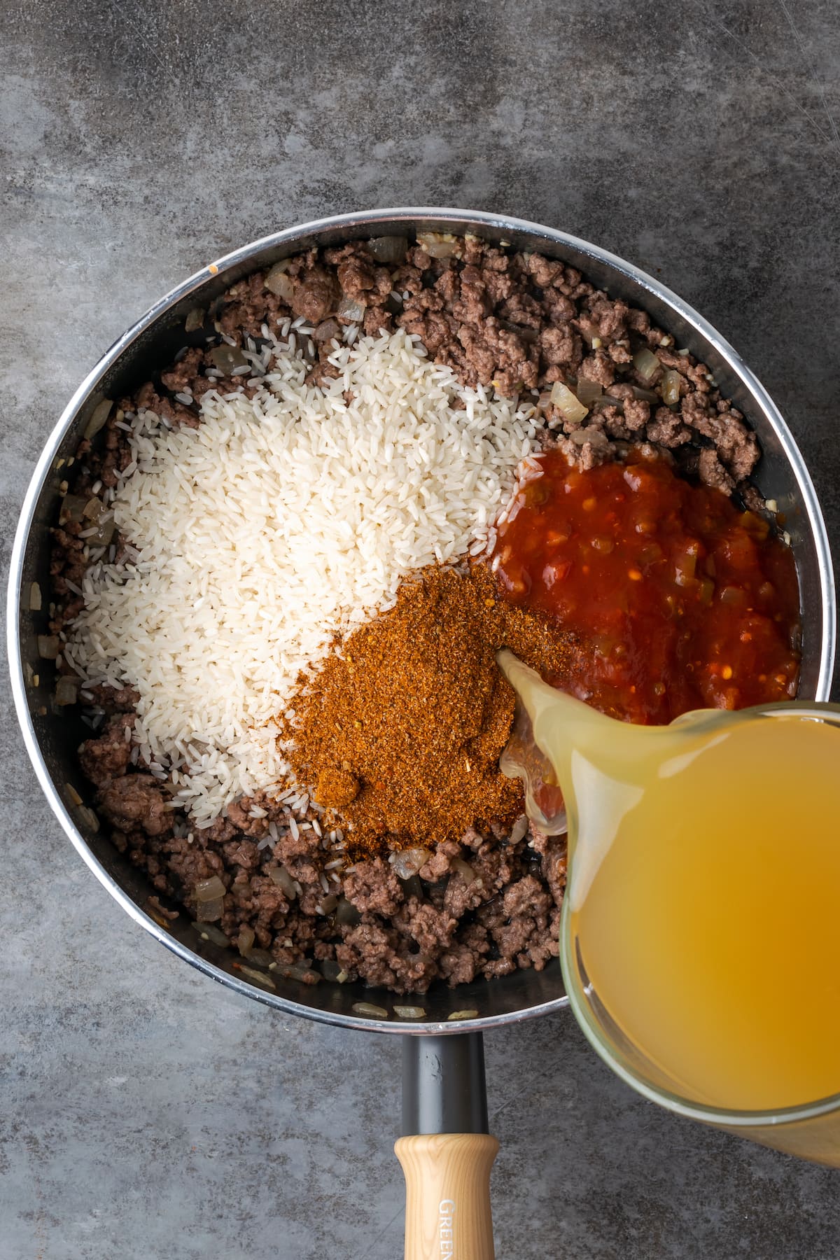 Chicken broth is poured into a skillet with ground beef, rice, salsa, and taco seasoning.