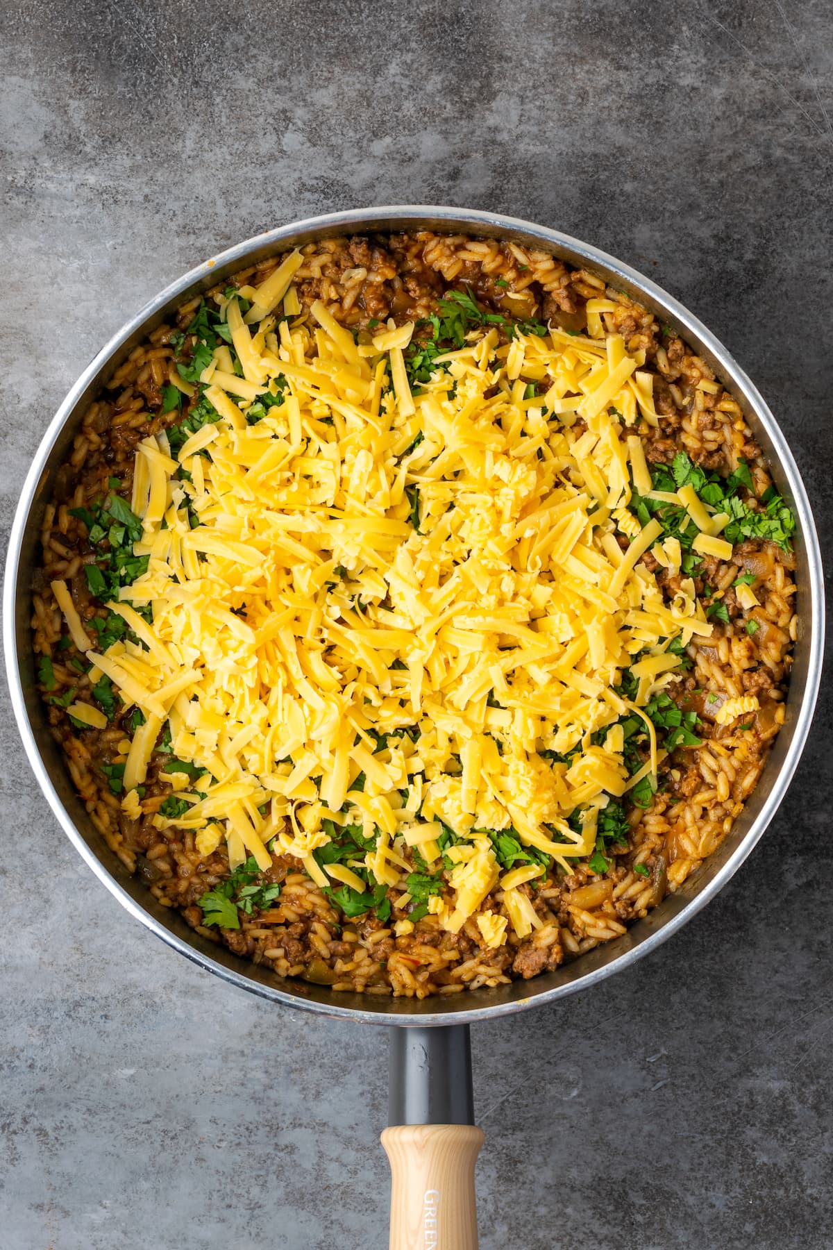 Cooked taco rice in a skillet topped with cilantro and shredded cheese.