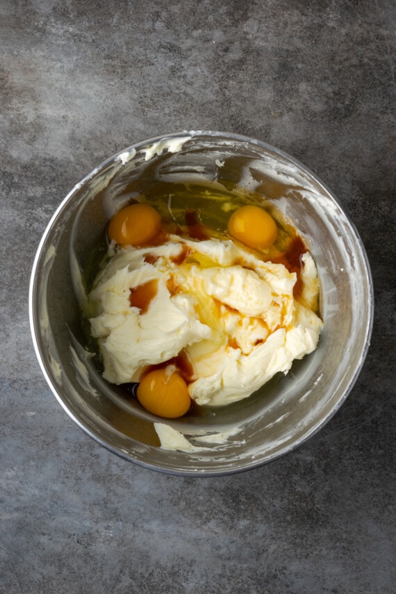 Eggs and vanilla added to beaten cream cheese in a mixing bowl.