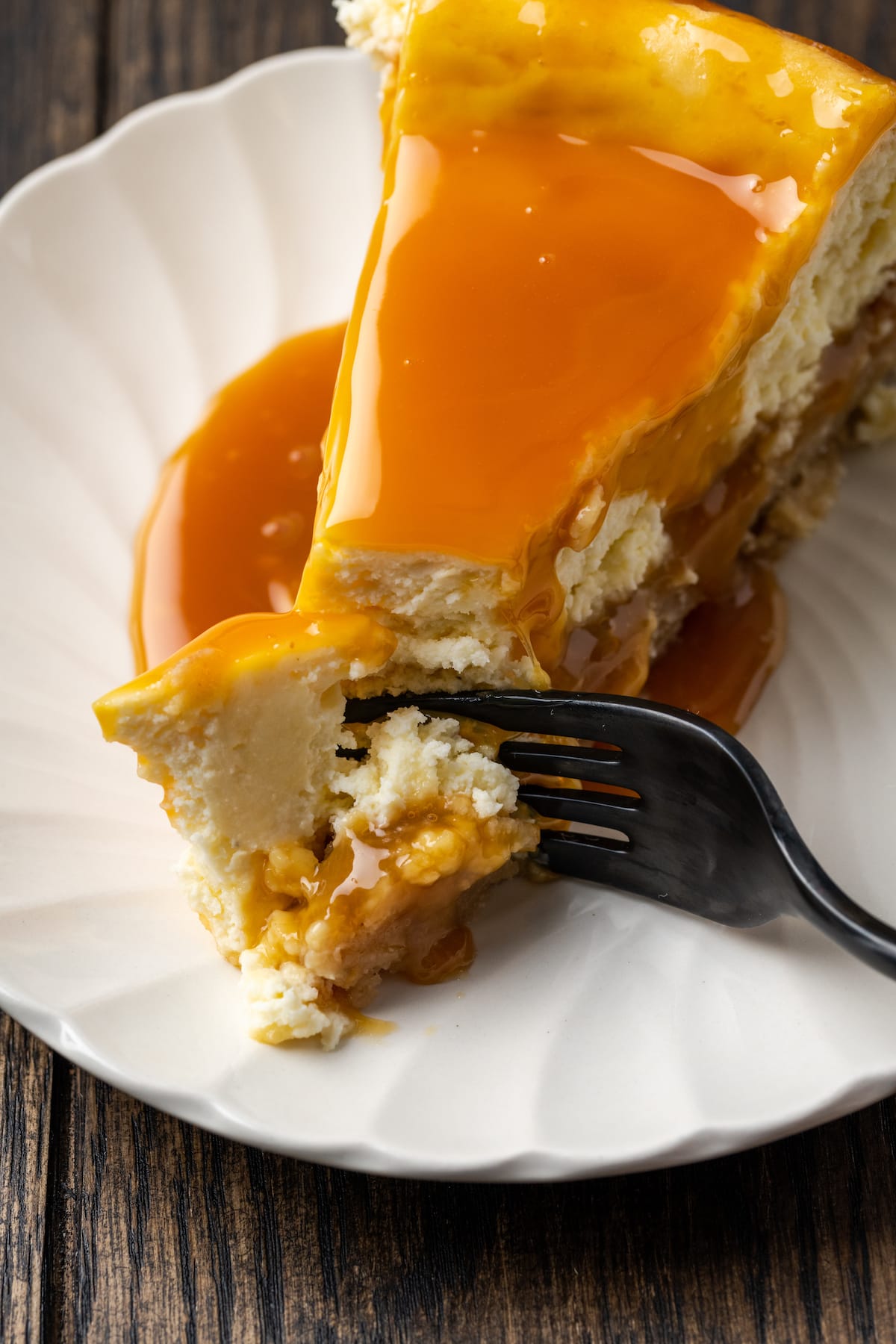 A fork cuts into the tip of a slice of caramel-soaked banana blondie cheesecake on a white plate.