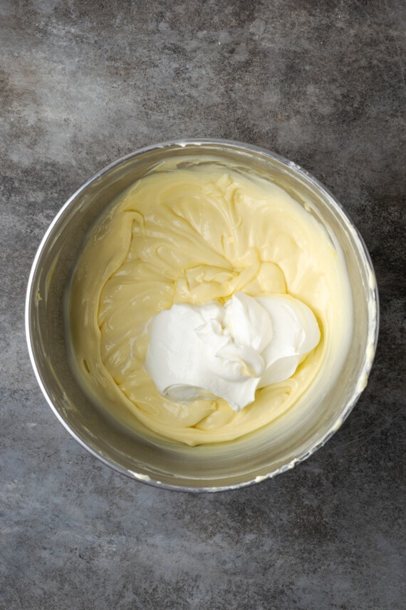 Sour cream added to cheesecake batter in a mixing bowl.