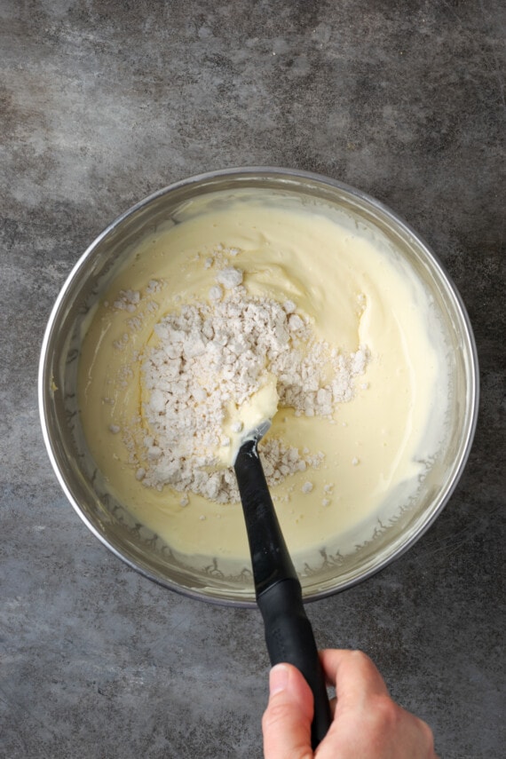Flour is stirred into cheesecake batter in a mixing bowl.