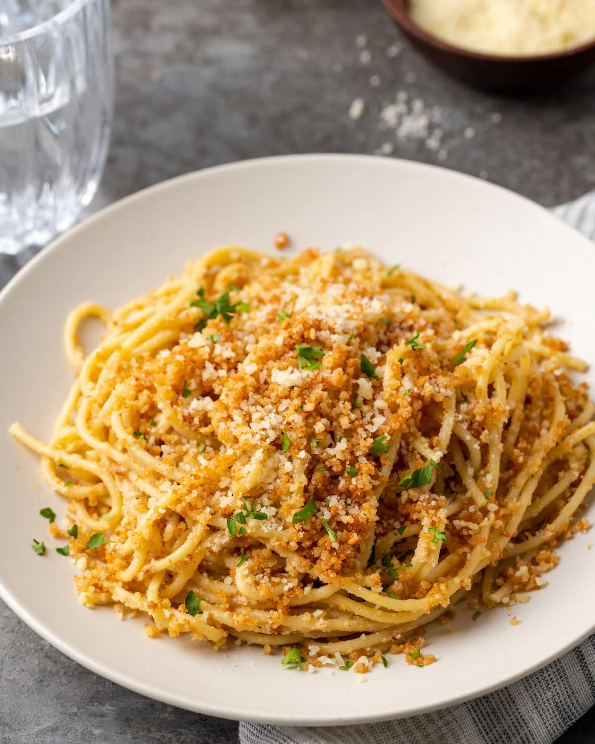 A serving of Caesar pasta on a white plate topped with garlic breadcrumbs and parsley.