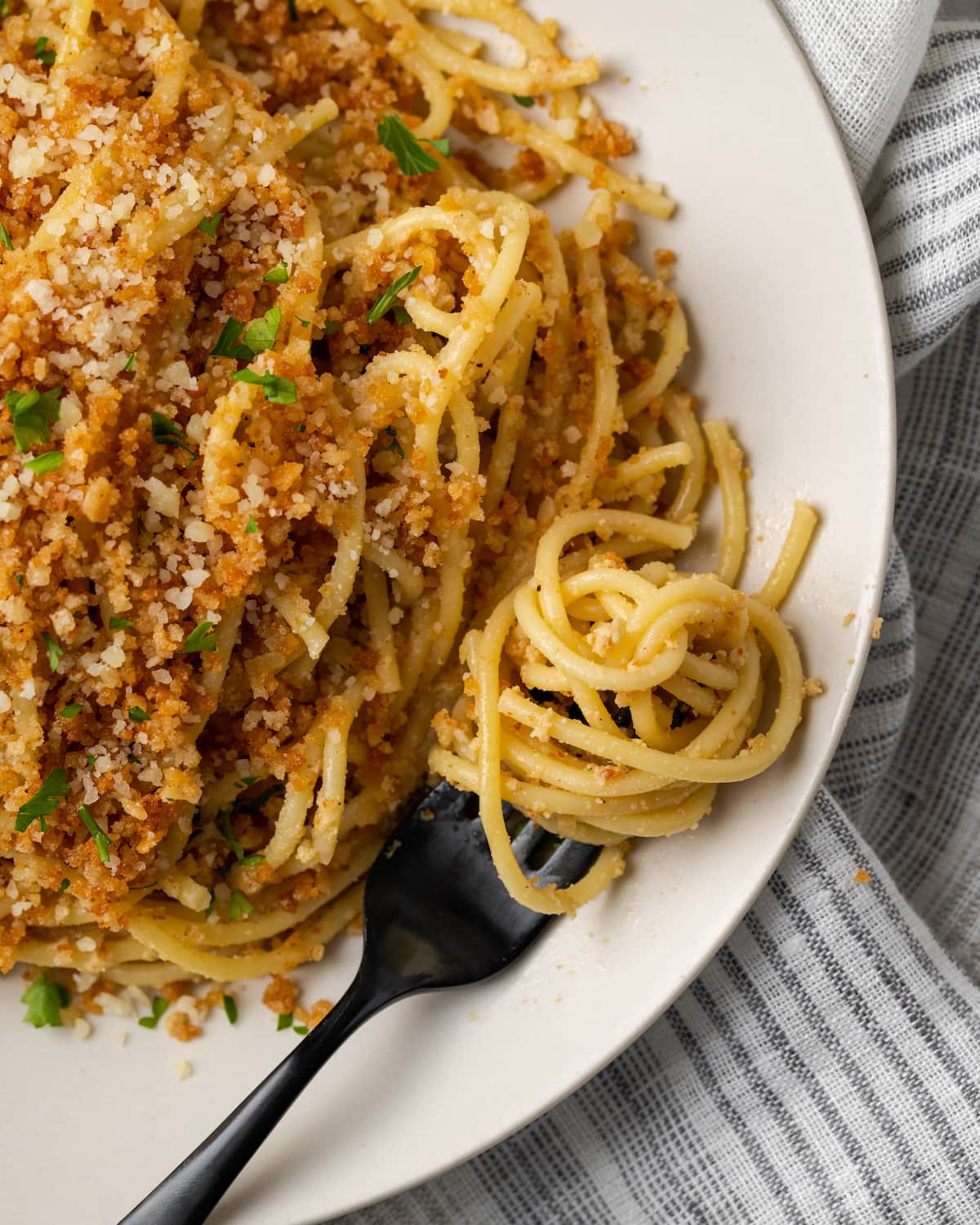 Overhead view of Caesar pasta on a white plate topped with garlic breadcrumbs and parsley, next to pasta swirled on a fork.