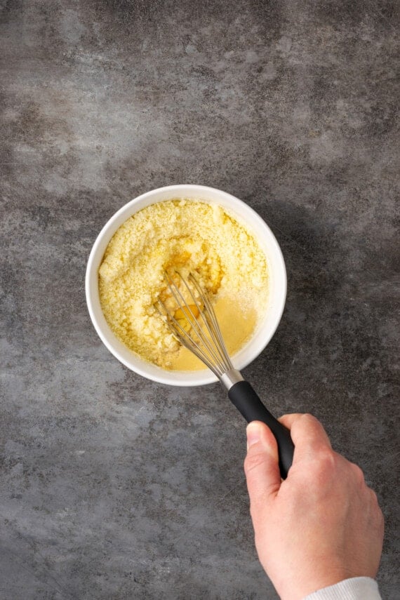 A hand using a whisk to combine Caesar pasta sauce ingredients in a bowl.