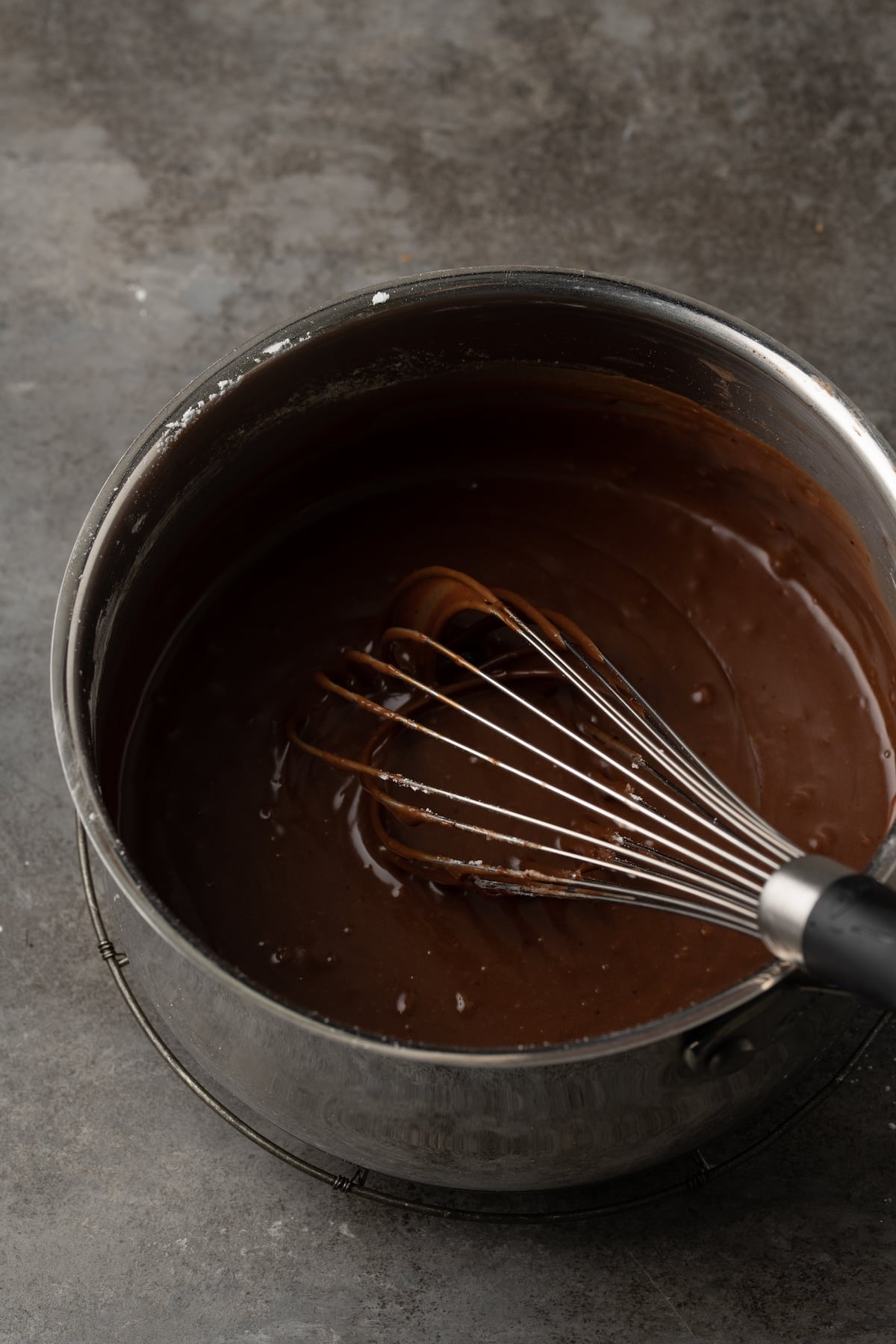 Chocolate icing in a saucepan with a whisk.