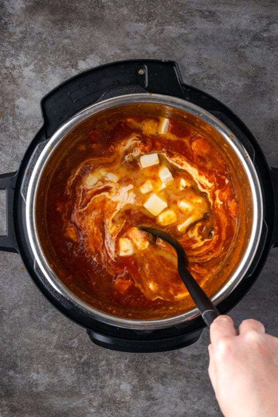 A hand uses a spoon to stir together butter chicken inside the instant pot.