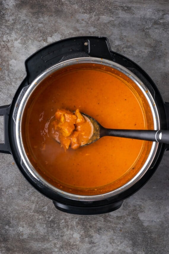 A spoonful of butter chicken held over the instant pot.