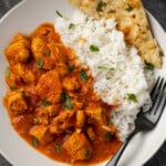 Overhead view of instant pot butter chicken served on a white plate next to a side of basmati rice and naan, garnished with fresh chopped cilantro.