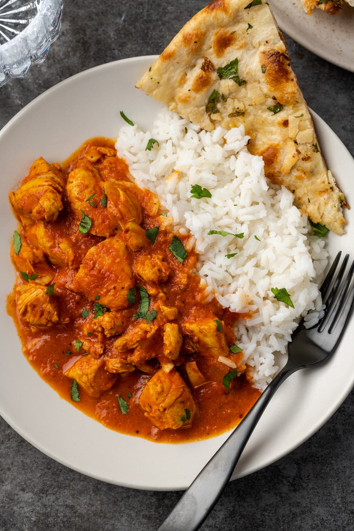 Overhead view of instant pot butter chicken served on a white plate next to a side of basmati rice and naan, garnished with fresh chopped cilantro.