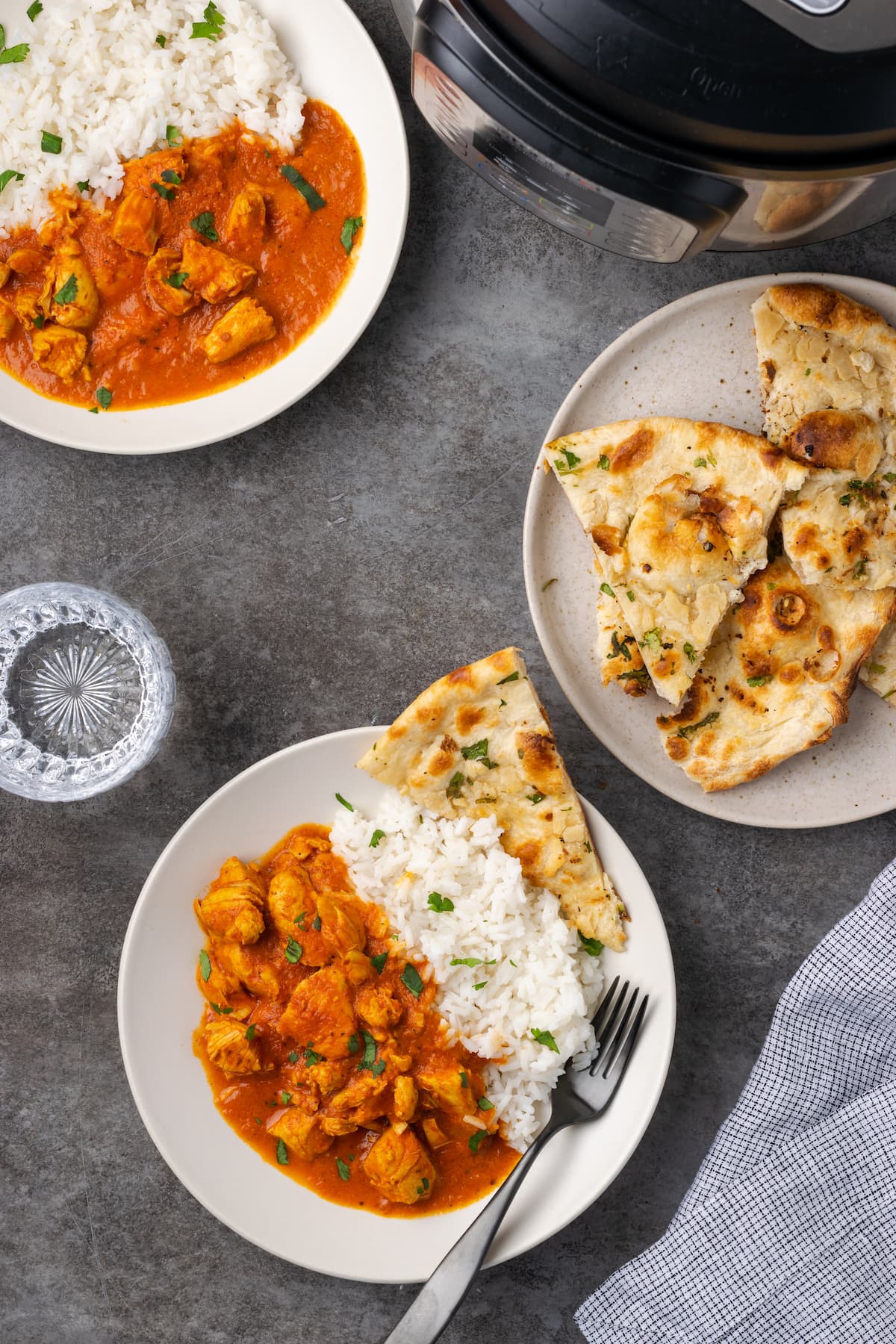 Overhead view of two plates filled with butter chicken and a side of rice, next to a plate of naan and the Instant Pot.