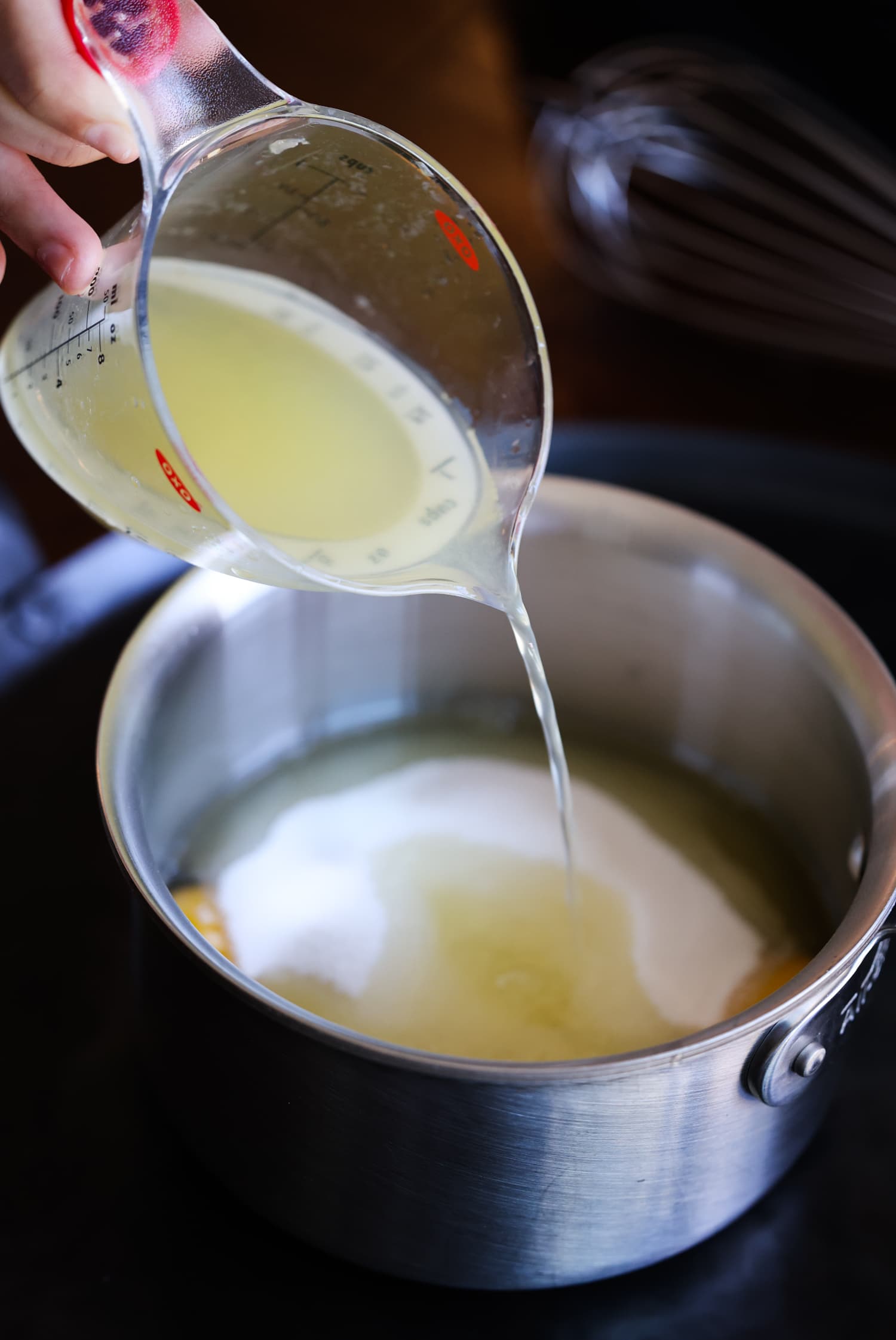 pouring lemon juice into a saucepan with granulated sugar