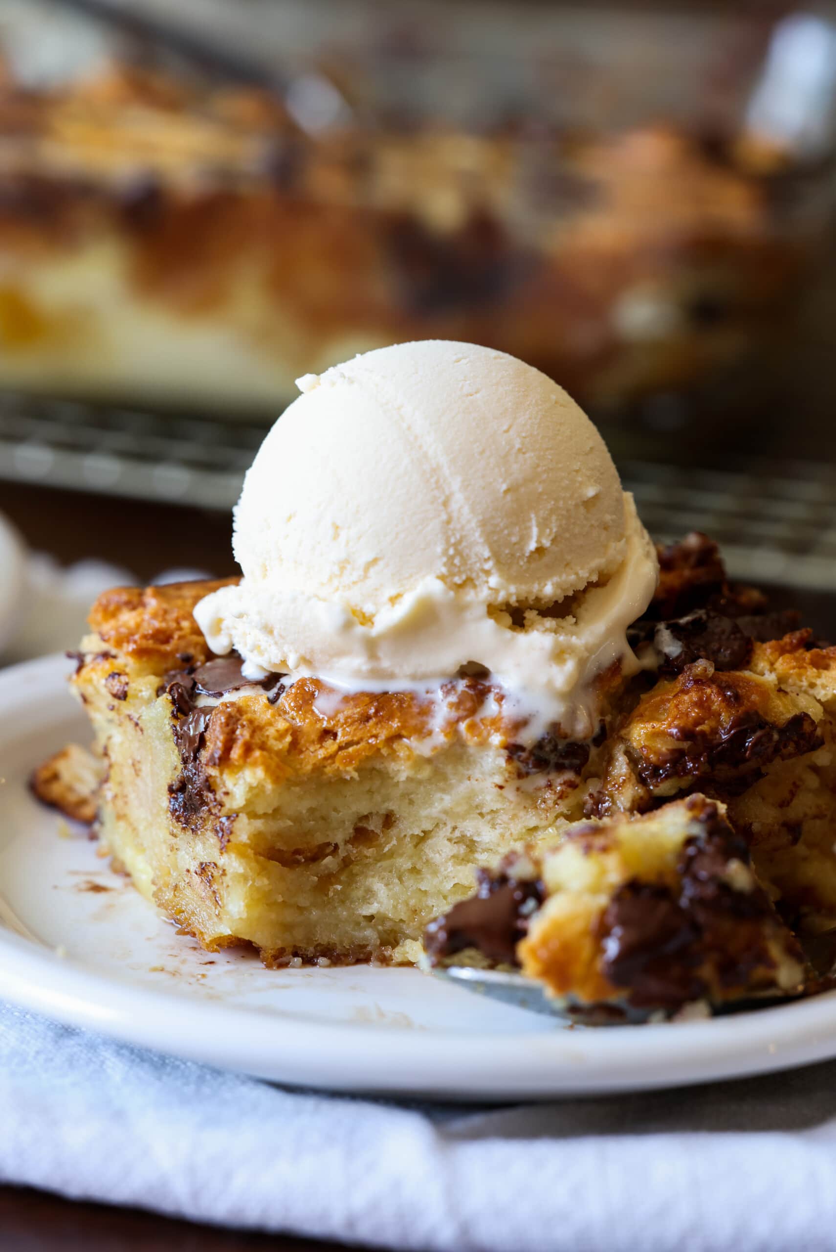 A piece of biscuit bread pudding on a plate with ice cream from which a spoon is taken