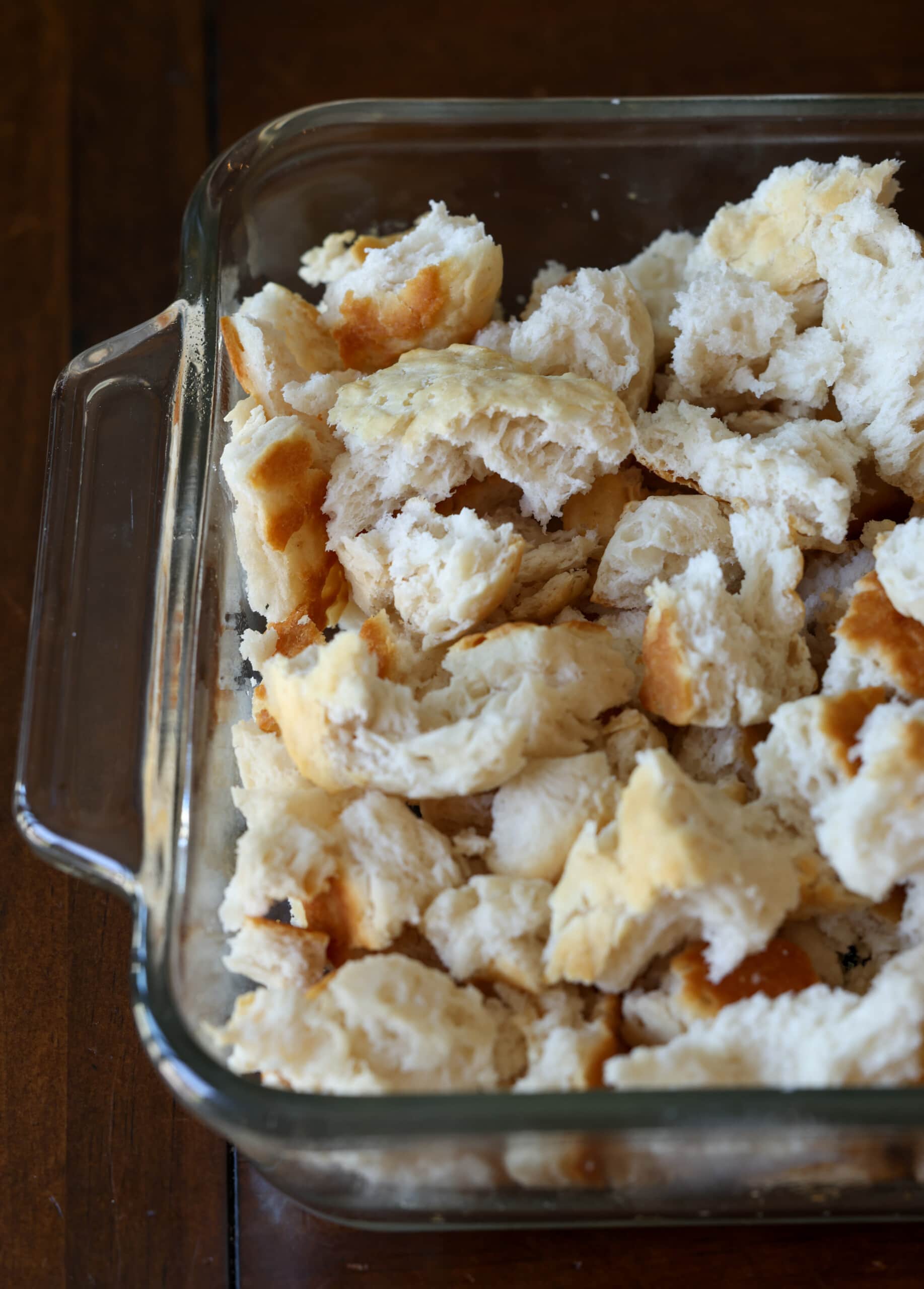 Torn and crumbling day-old biscuits in an 8x8 glass baking pan