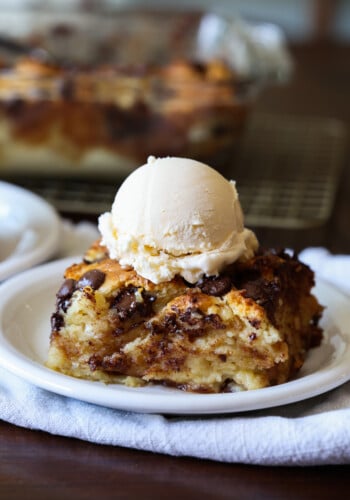 A piece of bread pudding made with day old biscuits on a white plate with vanilla ice cream.