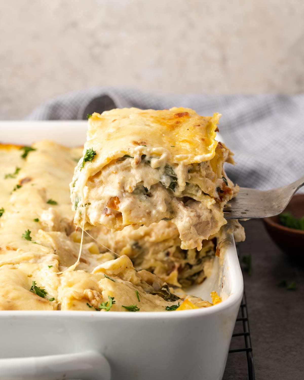 A slice of chicken lasagna is lifted from a casserole dish.