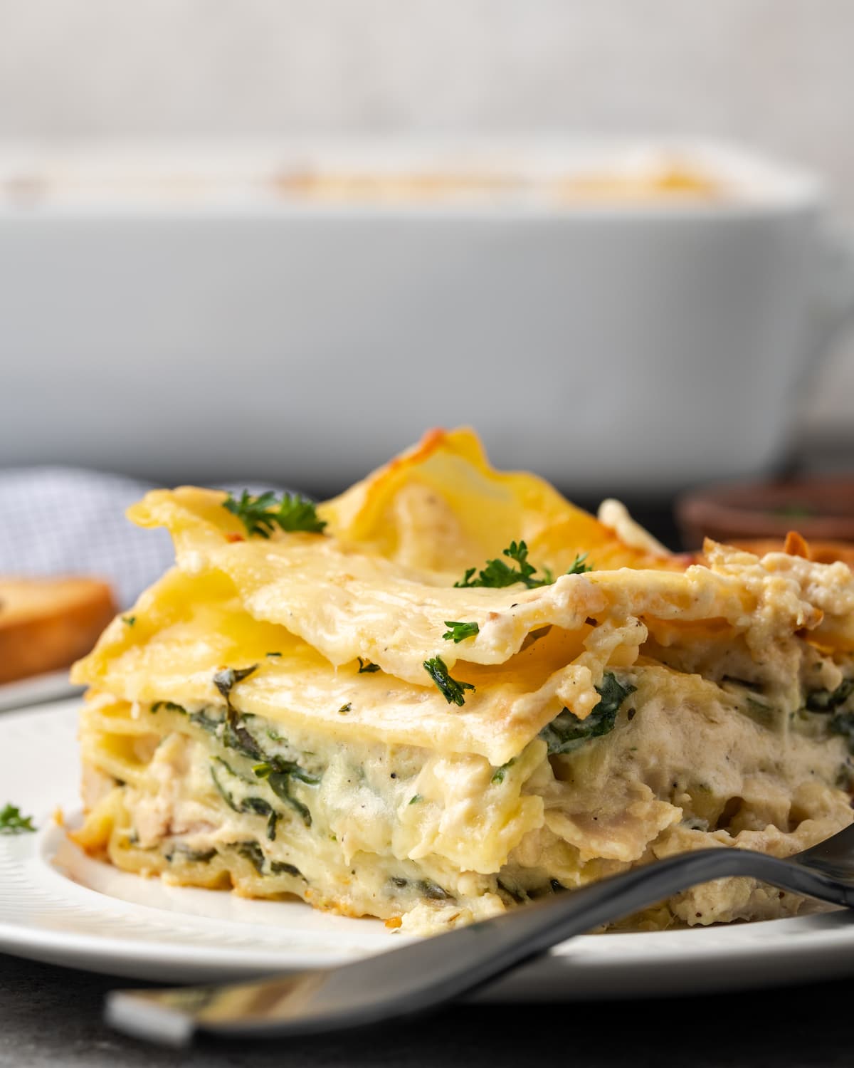 A serving of chicken lasagna on a plate next to a fork.