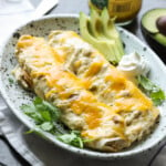 Chicken Enchiladas on a serving plate covered in melted cheese with avocado slices