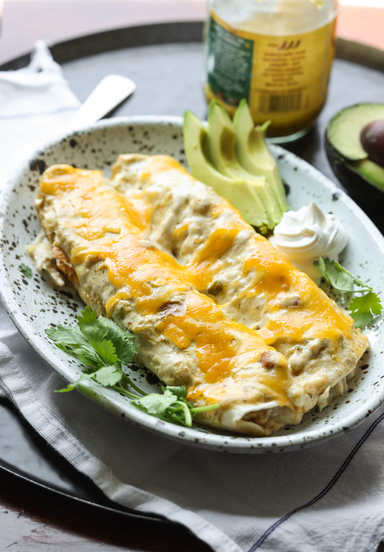 Chicken enchiladas served on a plate covered in melted cheese with avocado slices