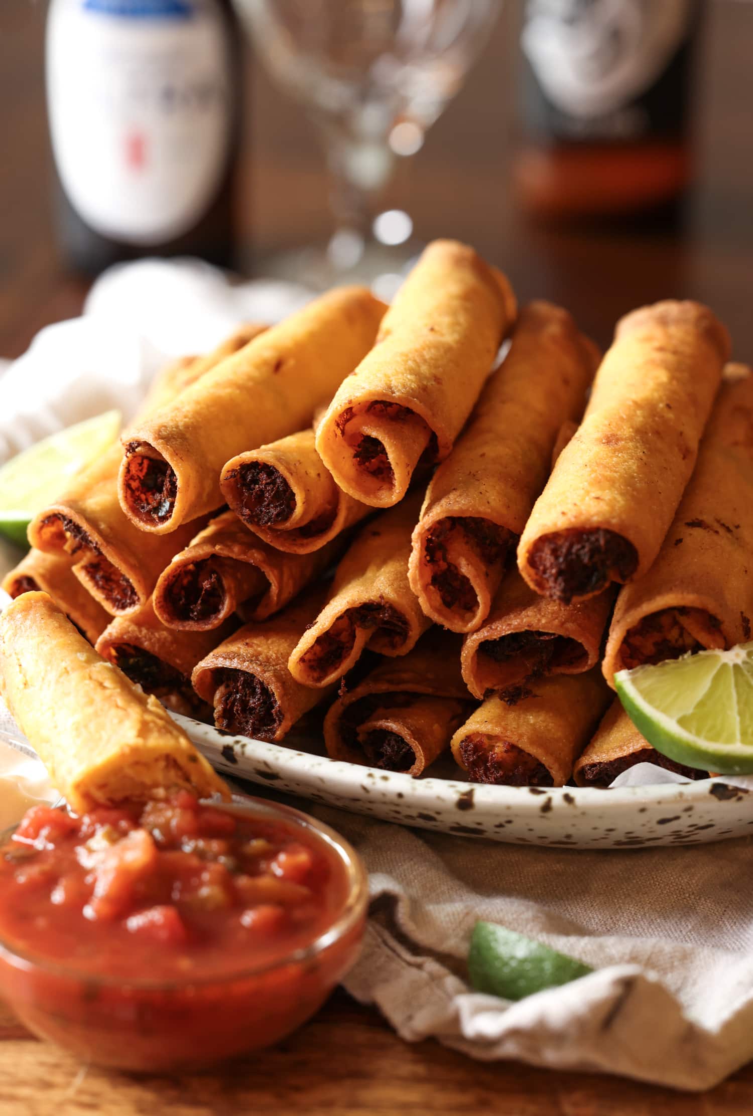taquitos on a platter with salsa and lime wedges with beer 
