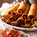 chicken taquitos piled on a platter with salsa to dip