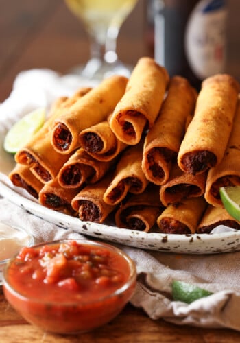 chicken taquitos piled on a platter with salsa to dip