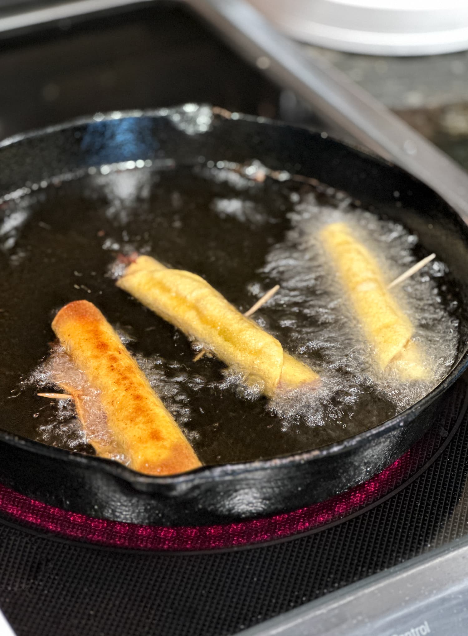 Frying chicken taquitos in a cast iron skillet