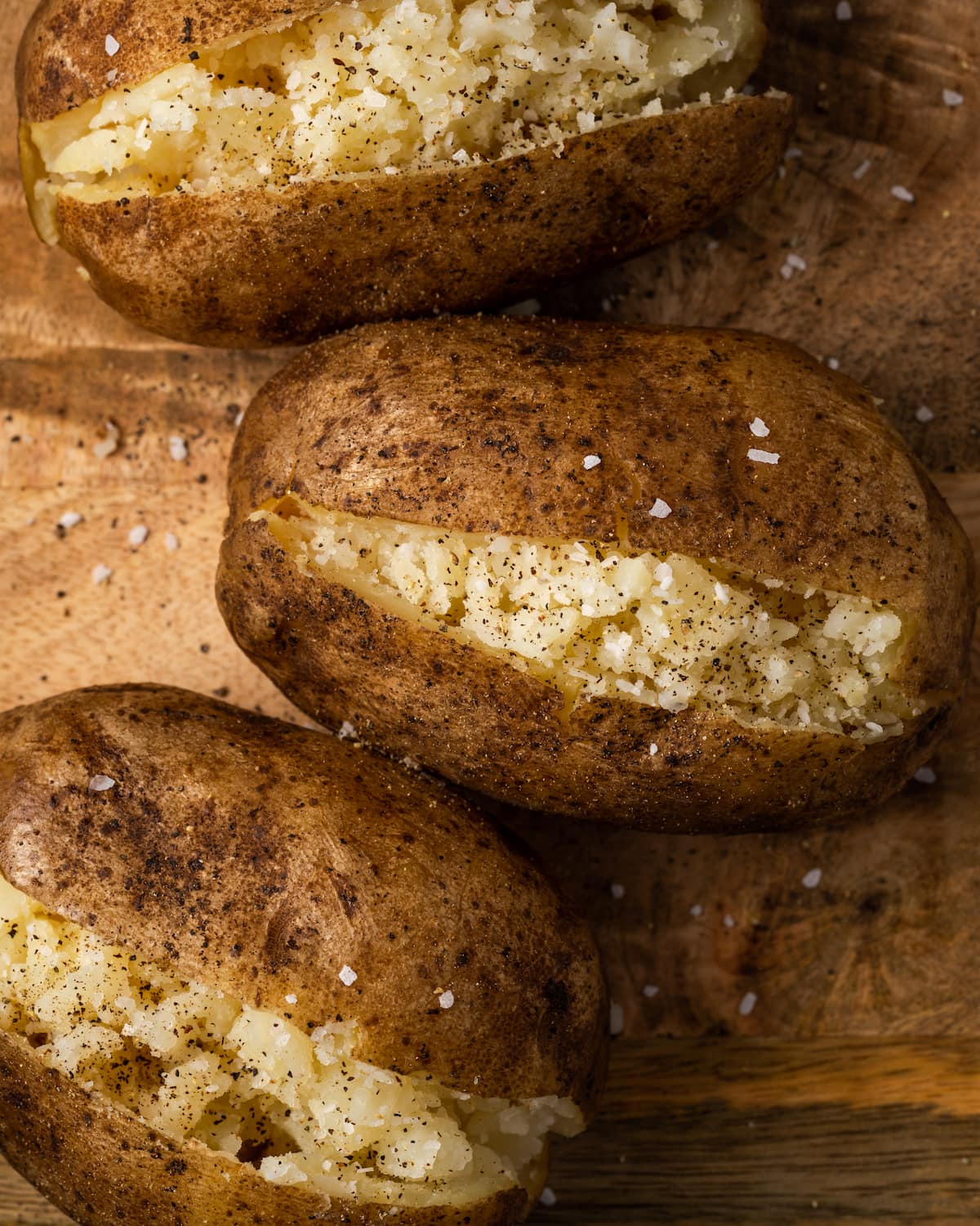 Close up of three crock pot baked potatoes on a wooden surface.