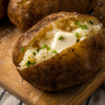 Close up of a crock pot baked potato topped with butter and chives on a wooden board.