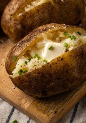 Close up of a crock pot baked potato topped with butter and chives on a wooden board.