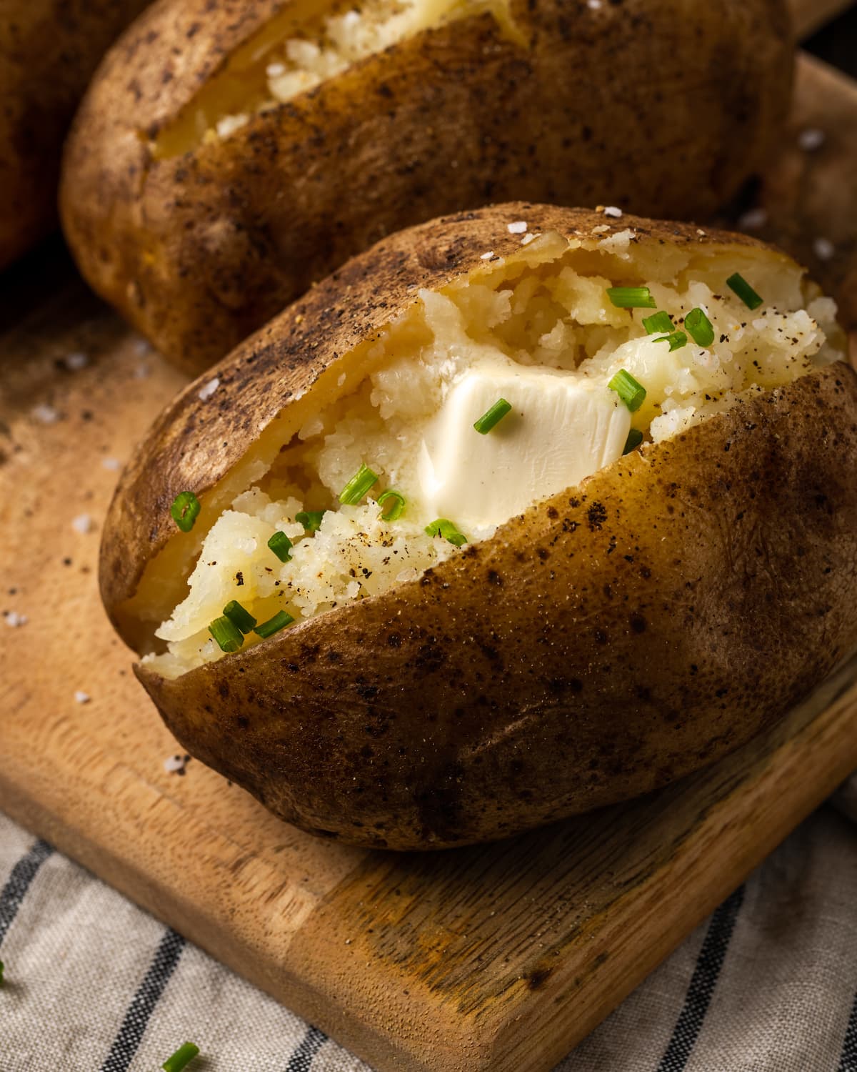 Close-up of a clay pot baked potato topped with butter and chives on a wooden board.
