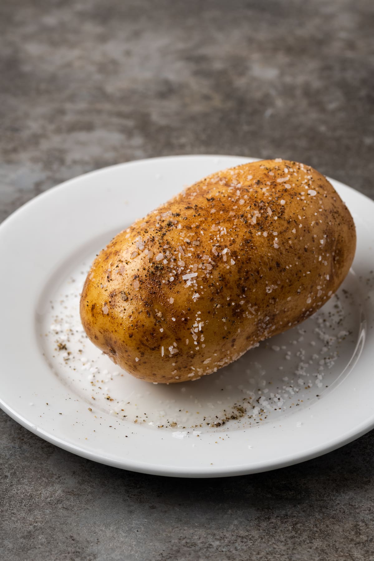 A potato seasoned with salt and pepper on a white plate.