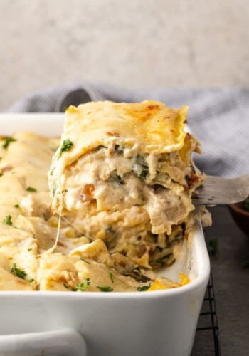 A slice of chicken lasagna is lifted from a casserole dish.