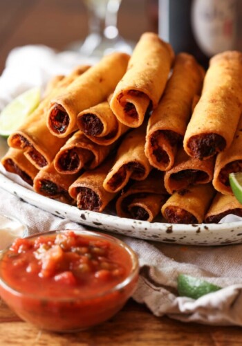 chicken taquitos piled on a platter with salsa to dip