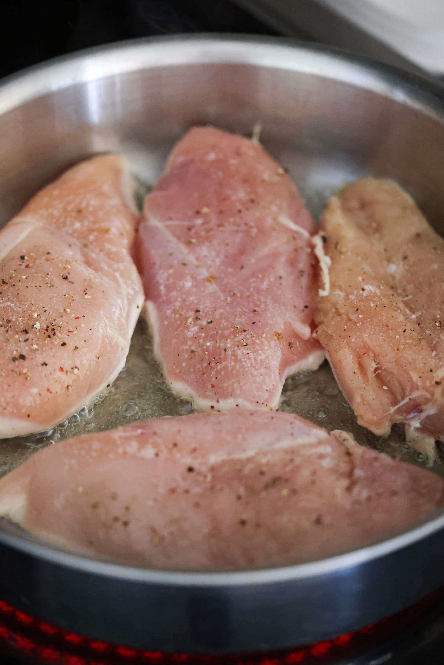 raw chicken breasts in a skillet cooked on one side