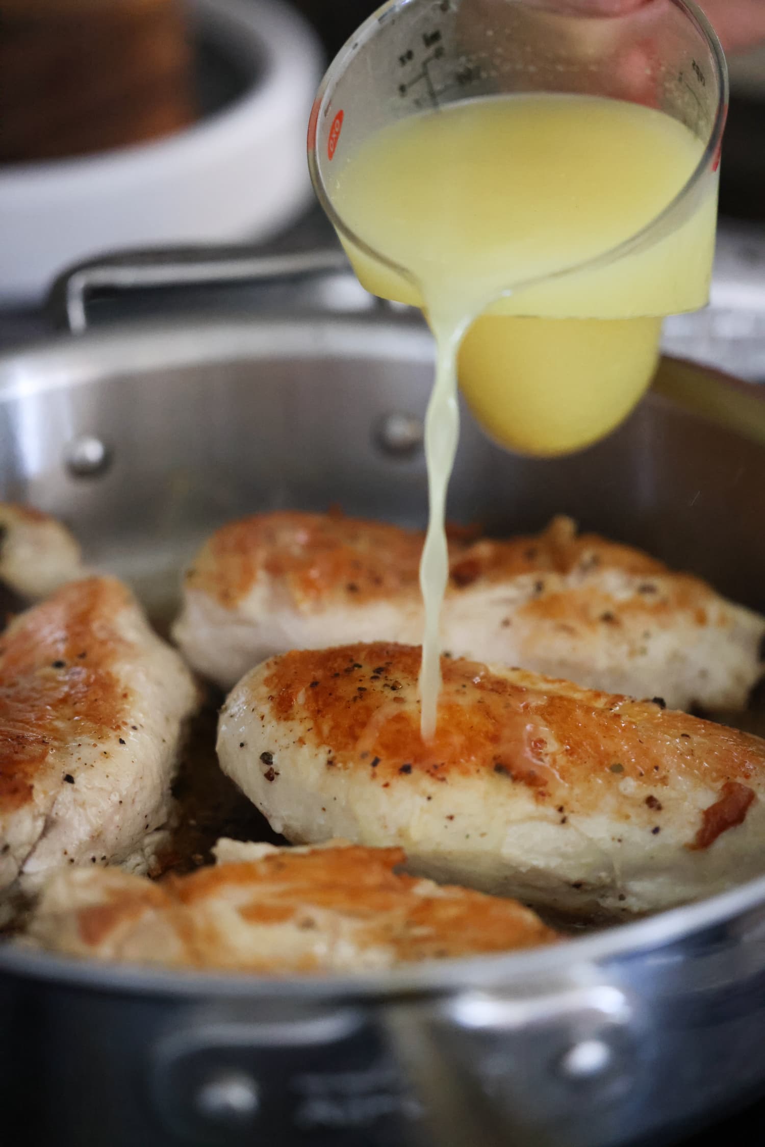 adding chicken broth into a skillet with chicken breasts