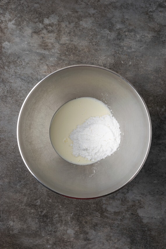 Powdered sugar and heavy cream combined in a metal bowl.