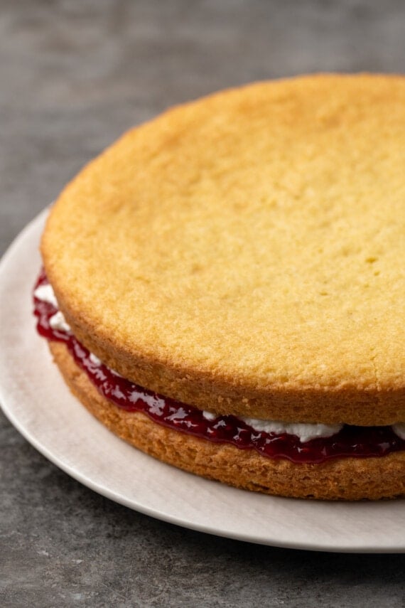 Assembled sponge cake layers filled with raspberry jam and whipped cream on a plate.
