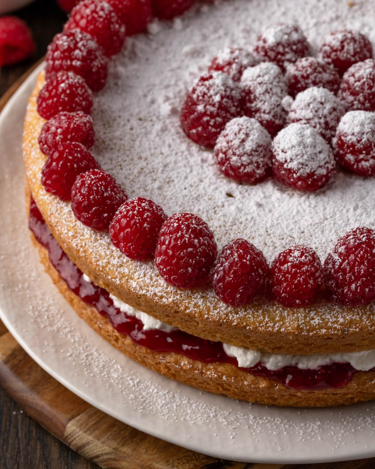 Victoria sponge cake dusted with powdered sugar and topped with fresh raspberries on a white plate.