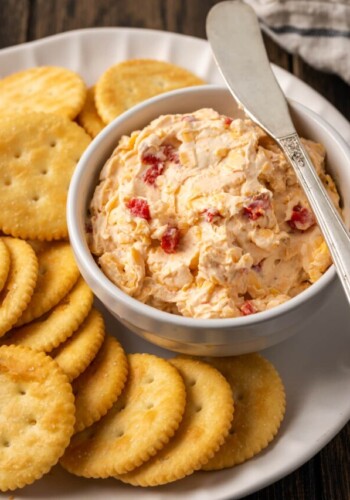 A bowl of pimento cheese served with a cheese knife on a platter of crackers.