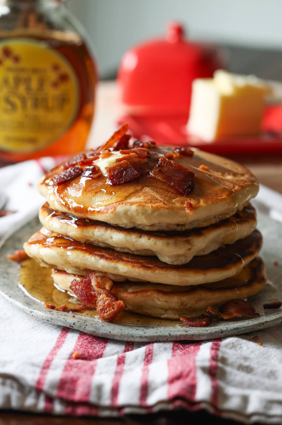 Stack of maple bacon pancakes topped with butter, chopped bacon and maple syrup