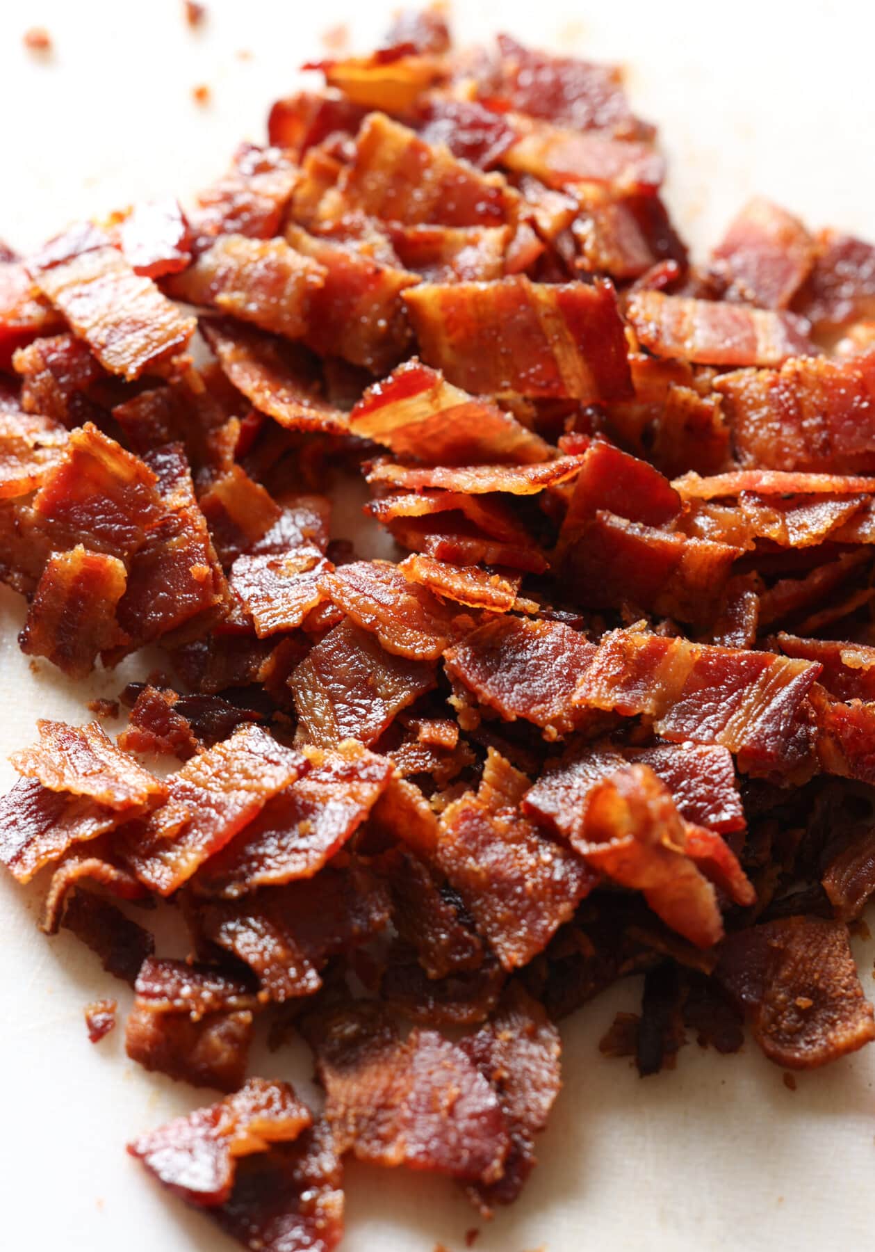 Maple Bacon Pancakes are fluffy buttermilk pancakes sweetened with brown sugar and maple syrup with crispy bacon bits inside and on top of the pancakes. chopped bacon on a white cutting board