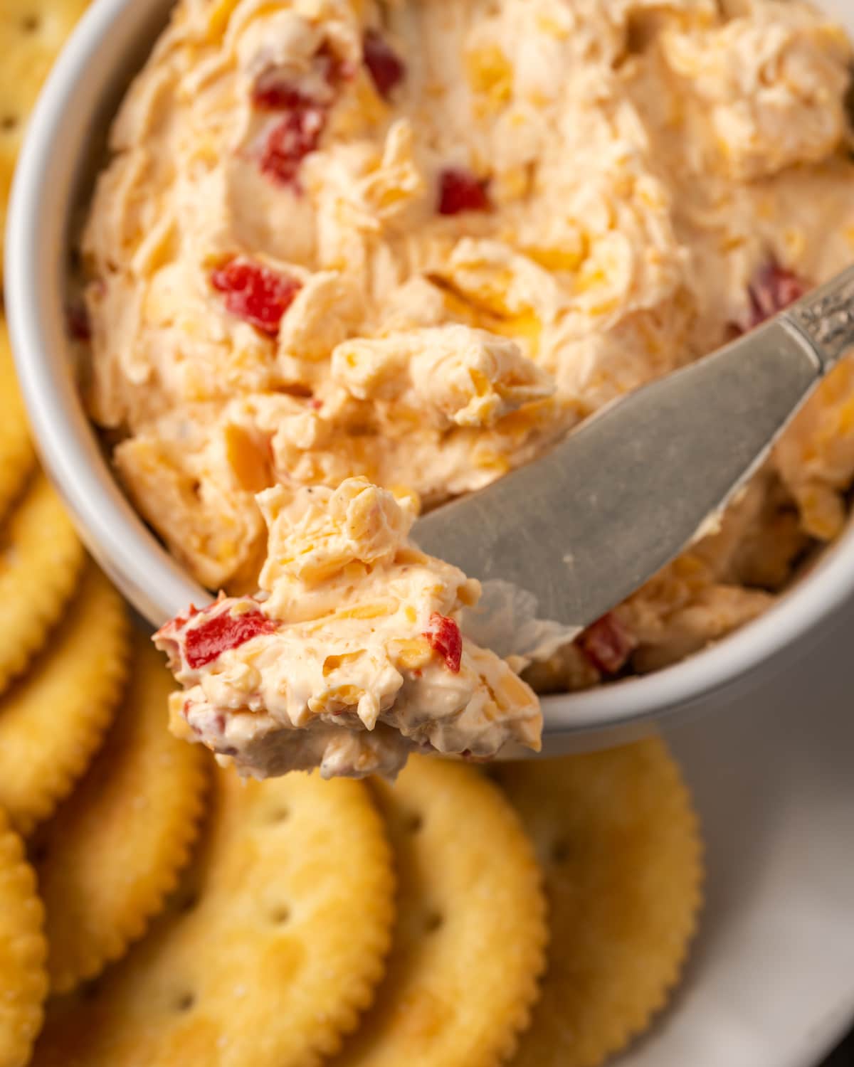 Close-up of a pimento cheese bowl served with a cheese knife on a cracker platter.
