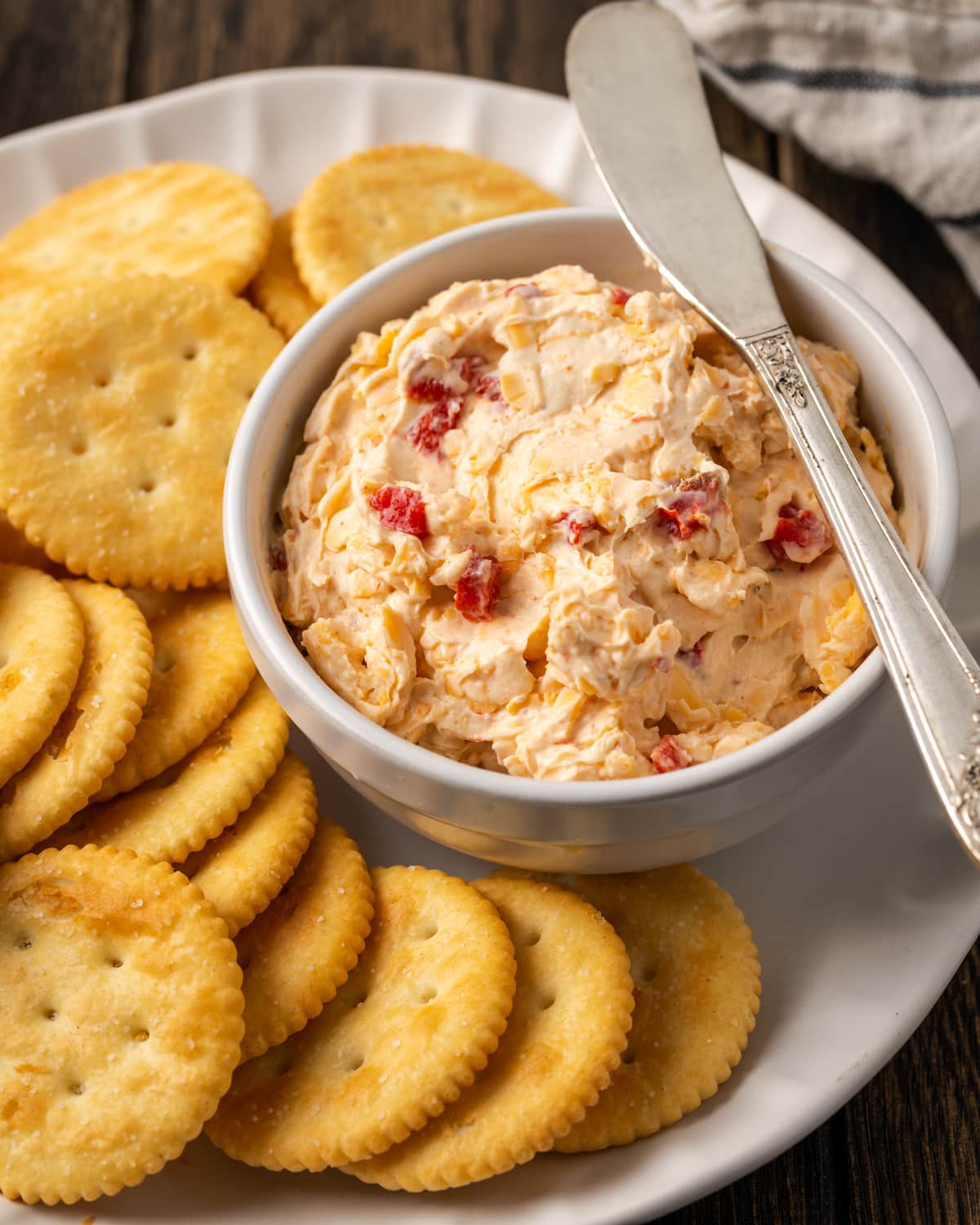 A bowl of pimento cheese served with a cheese knife on a cracker platter.
